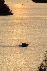 A motorboat speeds across a lake glowing with golden sunset reflections, creating a dynamic...