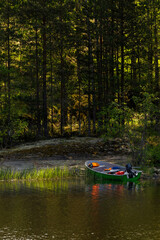 Small green motorboat with gear and life jackets moored at a quiet forest shoreline, ideal for...
