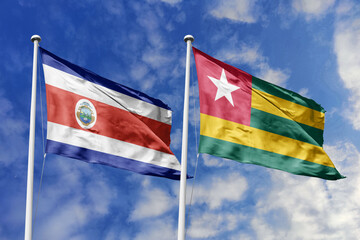 Costa Rica and Togo national flags waving in the wind against a blue sky, symbolizing international relations, diplomacy, and friendship between the two countries.