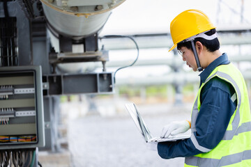Engineer is working on high voltage power substation infrastructure inspection using laptop to...
