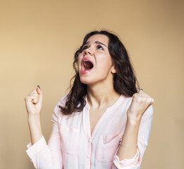 Emotional brunette woman screaming over beige background.