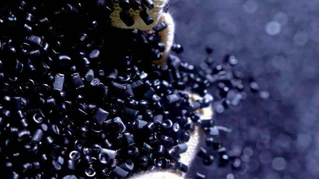 Polymer composite raw material pours in container for mixing.Concept ecological plastic recycling.4k slow motion pours plastic granules in product line.Top view on gloves with black plastic recycling
