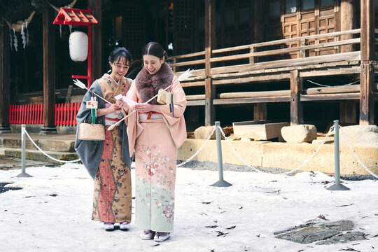 神社の境内でおみくじを見せ合う着物姿の日本人女性