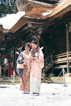 神社の境内でおみくじを見せ合う着物姿の日本人女性