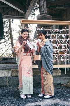 神社の境内でおみくじを見せ合う着物姿の日本人女性