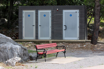 Modern public restroom facility with three doors, including accessible entrance, stands among rocks...