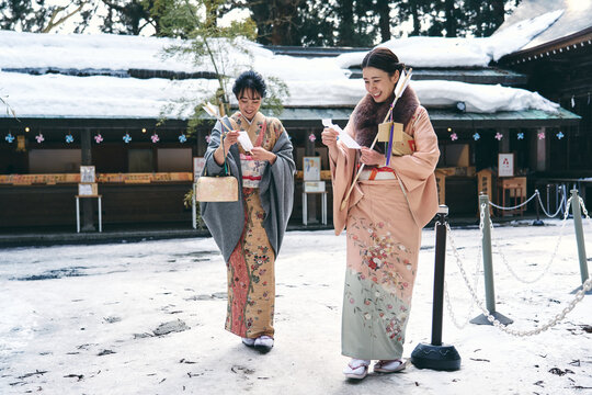 神社の境内でおみくじを見せ合う着物姿の日本人女性