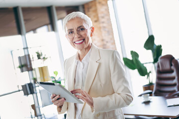 Confident senior businesswoman using a tablet in light modern office workspace, showcasing maturity...