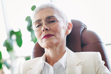 Elegant senior businesswoman relaxed in the workplace with eyes closed, exuding confidence and...