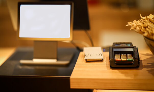Modern point-of-sale system with contactless payment terminal, RFID access scanner, and touchscreen monitor at a wooden reception or checkout counter