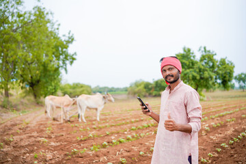young indian farmer holding smartphone standing in agriculture field