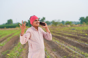 young indian farmer standing at agricultural field talking on smartphone