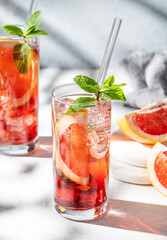 Two glasses of cocktail with grapefruit, mint and ice on a light trxtured background with shadow