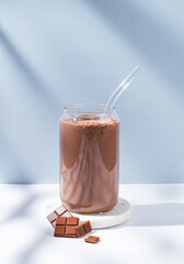 Chocolate smoothie with banana in a glass on a white blue background with morning shadow.