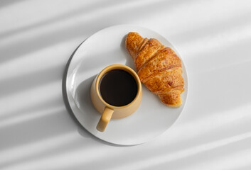Coffee espresso in yellow cup and fresh croissant on a plate on white background