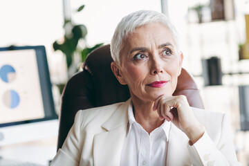 Elegant mature businesswoman in a formal suit sitting in a modern office contemplating a confident...