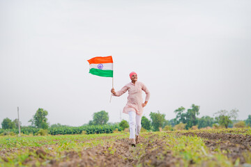 yong indian farmer holding indian flag standing at field