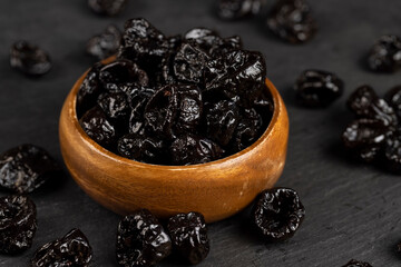 old bowl filled with dried prunes made from small plums, dark-colored dried plum fruits poured into...