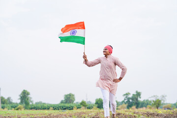 yong indian farmer holding indian flag standing at field