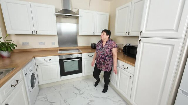 Excited woman dancing in kitchen, moving gracefully while enjoying upbeat rhythm. Gleeful dancer letting loose indulging in leisure at home. Joyful lady shifting weight with enthusiasm, fully absorbed