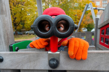 A boy looks through toy binoculars on the playground. in the cold autumn.