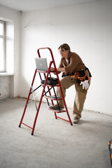 Female foreman or repairman using laptop on the ladder in light interior