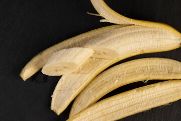 one open banana on a black slate board, ripe and sweet yellow banana on a kitchen board made of...