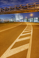 Bending road with road markings with illuminated oil refinery and storage tanks on background at night, port of Antwerp