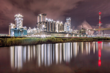 Busy illuminated petrochemical power plant at nighttime reflected in a large pond, Port of Antwerp, Belgium 