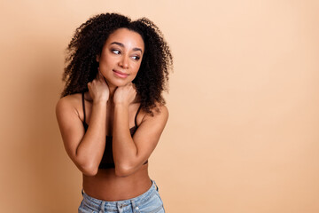 Fashionable young woman with curly hair posing in a casual top on a beige background