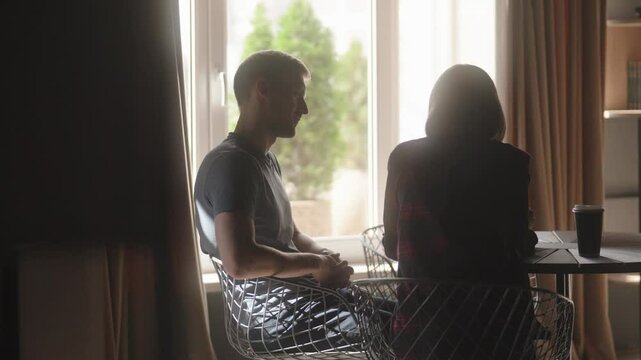 Couple in cafe talking, having a business meeting, backlit by sunlight.