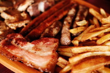 Close-up of grilled Balkan meat platter with sausages, bacon, and French fries. Serbian cuisine at a local restaurant.