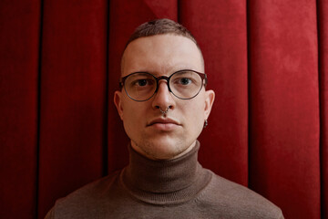 Portrait of young adult Caucasian man wearing glasses and nose ring looking directly at camera...