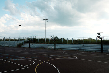 Empty outdoor basketball court with faded bleachers and cloudy sky above. Small Serbian town.