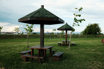 Multiple wooden picnic shelters in a park with grass and industrial background. Serbian town...