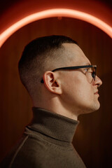 Caucasian young adult man with short hair and glasses standing in profile view wearing turtleneck,...
