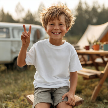 Summer camp kids model mockup. Boy wearing white shirt sitting at camping table, tent and camper van in background. Kids blank short sleeve t-shirt template. Children's casual tee mockup	
