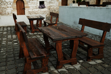 Rustic wooden benches and tables arranged in a stone-paved courtyard against a medieval stone wall with arched doors and flowers. Serbia country.