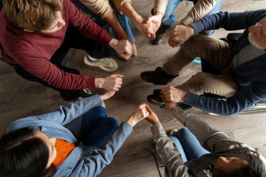 Diverse group of people holding hands in circle during support meeting