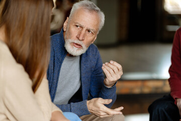 Senior man gesturing while talking with people during group therapy session