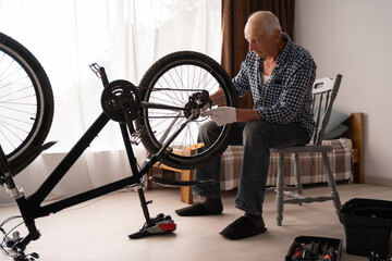Old man cyclist repairing his bike at home. DIY concept