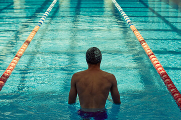A swimmer, wearing a cap and goggles in an indoor pool, is preparing for a race with clear lanes...