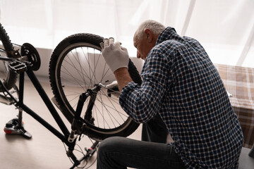 Retired Active man repairing bicycle at home. bike maintenance with wrench.