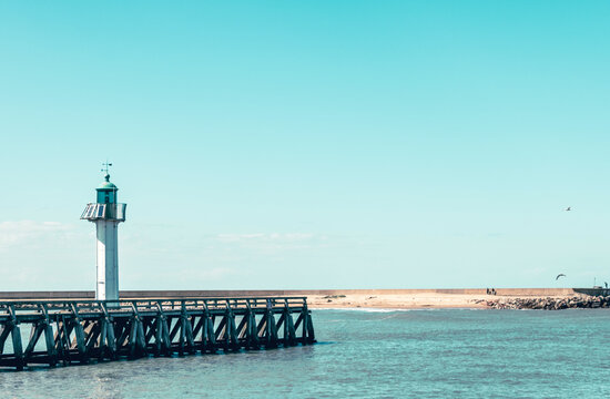 Scenic view of a lighthouse near a wooden pier under clear blue skies in a coastal location