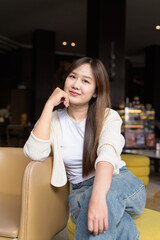 Fototapeta premium Young Asian woman sitting in cafe restaurant smiling and looking at camera