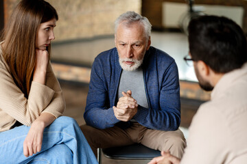 Senior man talking with psychologist and worried woman during therapy session