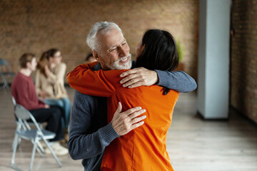Senior man and young woman hugging each other during group therapy session