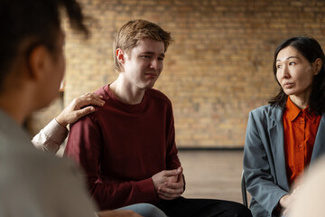 Psychologist comforting young man during group therapy session