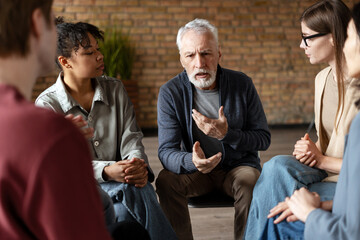 Senior man leading group therapy session, discussing problems and sharing experiences