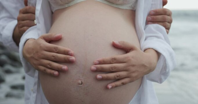 Young couple having tender moment with pregnant belly together on the beach - Family, maternity and pregnancy concept